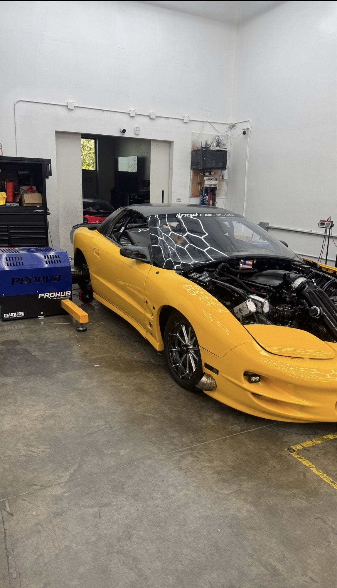 Yellow Camaro with engine bay exposed inside the shop